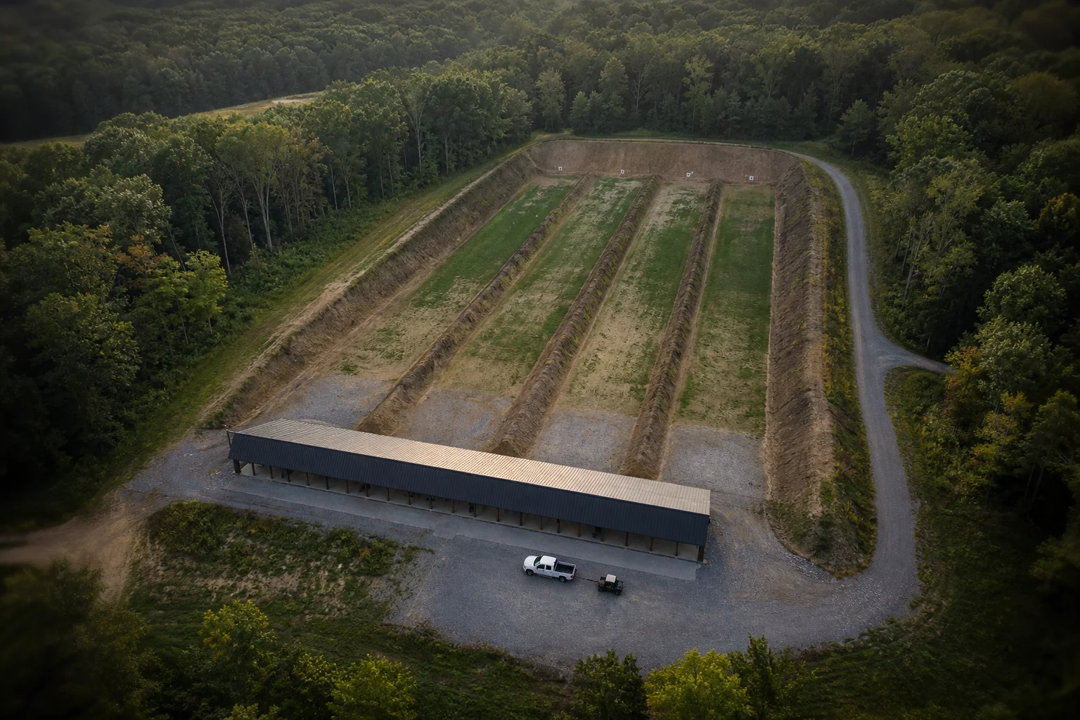 Aerial view of an outdoor shooting range with a covered firing line, divided bays and earthen impact berms